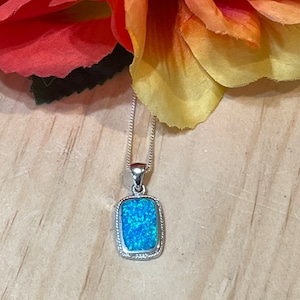 May include: A silver chain necklace with a rectangular pendant featuring a blue opal stone.
