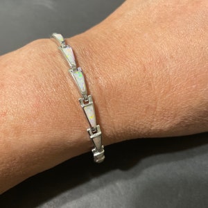May include: A silver bracelet with white opal stones set in a geometric pattern.