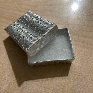 May include: A silver gift box with a textured lid and a white velvet interior.