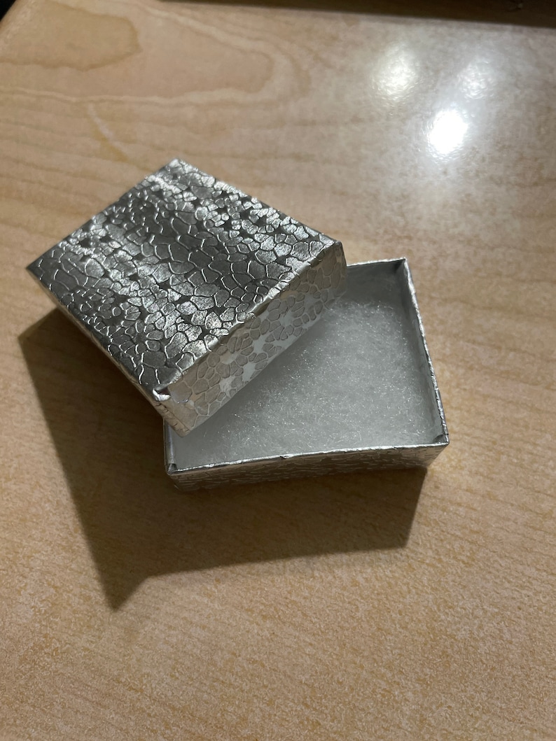 May include: A silver gift box with a textured lid and a white velvet interior.