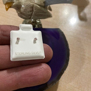 May include: A pair of sterling silver earrings with small pink stones. The earrings are on a white card with the words "Sterling Silver" printed on it.