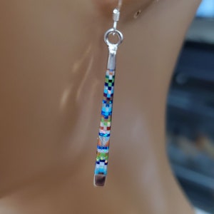May include: A pair of silver dangle earrings with a geometric pattern of blue, green, white, and brown squares. The earrings are long and slender.