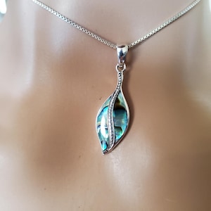 May include: Silver necklace with a leaf-shaped pendant. The pendant features a shimmering, iridescent abalone shell inlay, framed by a silver border with small, clear stones. The chain is a delicate, box-style design.