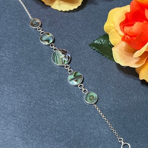 May include: A silver chain bracelet with five round abalone shell charms. The charms have a green, blue, and brown iridescent pattern.