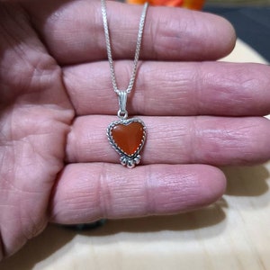 May include: A silver chain necklace with a heart-shaped pendant featuring a carnelian stone.