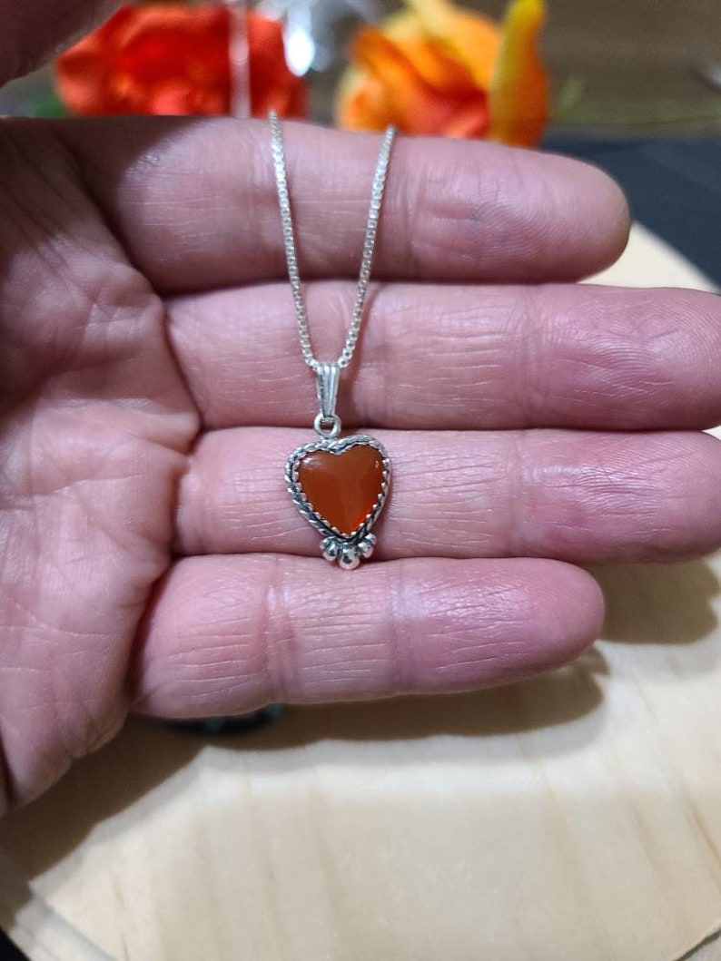 May include: A silver chain necklace with a heart-shaped pendant featuring a carnelian stone.