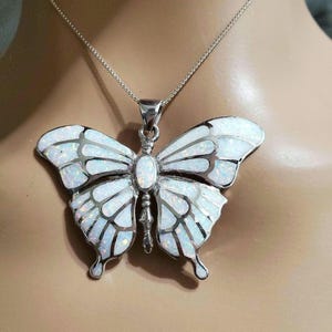 May include: A silver butterfly pendant necklace with a white and iridescent opal-like design. The butterfly has detailed wing patterns and is suspended from a delicate silver chain. The pendant is a statement piece.