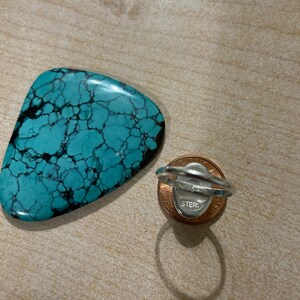 May include: A turquoise ring with a silver band and a sterling silver stamp on the back. The ring is sitting on a penny.