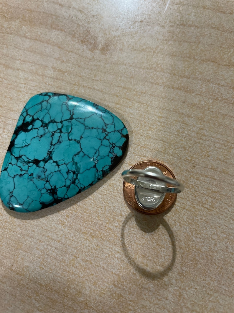 May include: A turquoise ring with a silver band and a sterling silver stamp on the back. The ring is sitting on a penny.