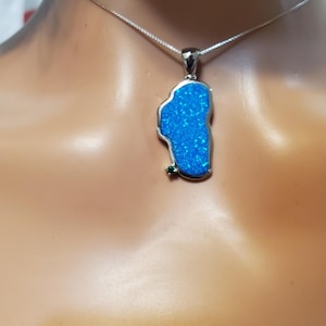 May include: A silver-toned necklace featuring a pendant shaped like the outline of Lake Tahoe. The pendant is filled with a vibrant, iridescent blue inlay and accented with a single small, round green gemstone at the bottom left corner.