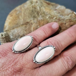 May include: Two silver rings with oval-shaped pink stones set in a rope-like design.
