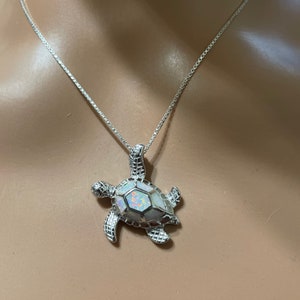 May include: A silver chain necklace with a silver turtle pendant. The turtle's shell is made of iridescent white opal.