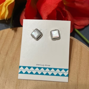 May include: A pair of silver earrings with white mother of pearl square stones. The earrings are displayed on a white card with the text "Sterling Silver" printed on it.
