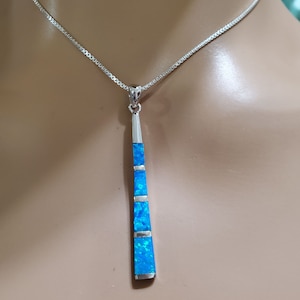 May include: A silver chain necklace with a pendant featuring a long, thin, blue opal stone with silver accents.