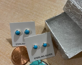 May include: A pair of sterling silver earrings with turquoise stones. The earrings are displayed on a white card with the word "STERLING" printed on it. A penny is also visible in the image.