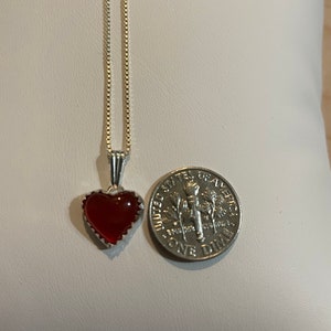 May include: A silver chain necklace with a red heart pendant. The pendant is about the size of a dime.