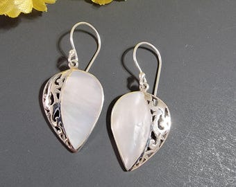 May include: A pair of silver earrings with a teardrop shape. Each earring features a pearly white, oval-shaped stone set within a silver filigree design. The earrings have a hook closure.