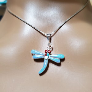 May include: A silver chain necklace with a dragonfly pendant. The dragonfly is made of blue opal and has red and white accents.