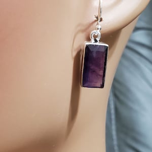 May include: A pair of silver earrings with a rectangular amethyst gemstone. The earrings have a simple design and are perfect for everyday wear.