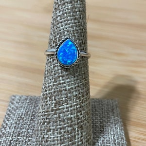 May include: A silver ring with a teardrop-shaped blue opal stone set in a silver bezel. The ring has a textured band.
