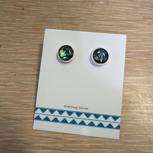 May include: A pair of sterling silver stud earrings with iridescent abalone shell insets. The earrings are displayed on a white card with a blue geometric border and the text "Sterling Silver".