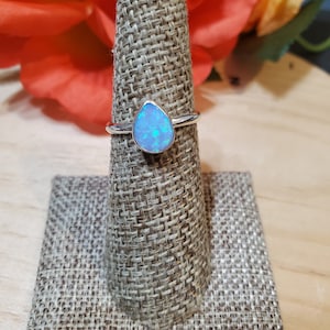May include: A silver ring with a teardrop-shaped blue opal gemstone.