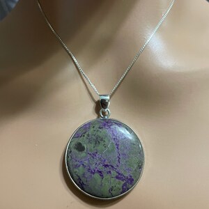 May include: A silver chain necklace with a round pendant featuring a green and purple marbled stone.