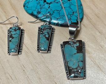 May include: A turquoise and sterling silver necklace and earrings set. The pendant and earrings feature a rectangular turquoise stone with a brown matrix. The necklace has a silver chain.