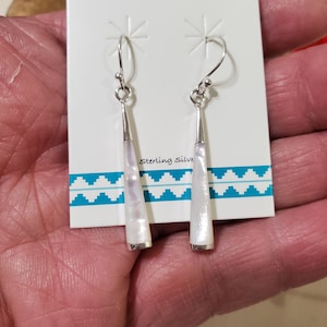 May include: A pair of dangle earrings with white mother of pearl teardrop shaped stones and sterling silver hooks. The earrings are displayed on a white card with the text "Sterling Silver" printed on it.