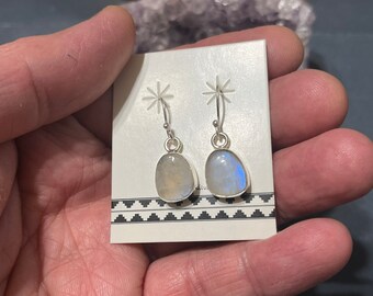 May include: A pair of silver dangle earrings with oval-shaped moonstone gemstones. The earrings have a simple design and are perfect for everyday wear.