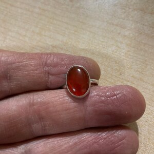 May include: A silver ring with an oval-shaped carnelian gemstone. The gemstone is a deep orange color.