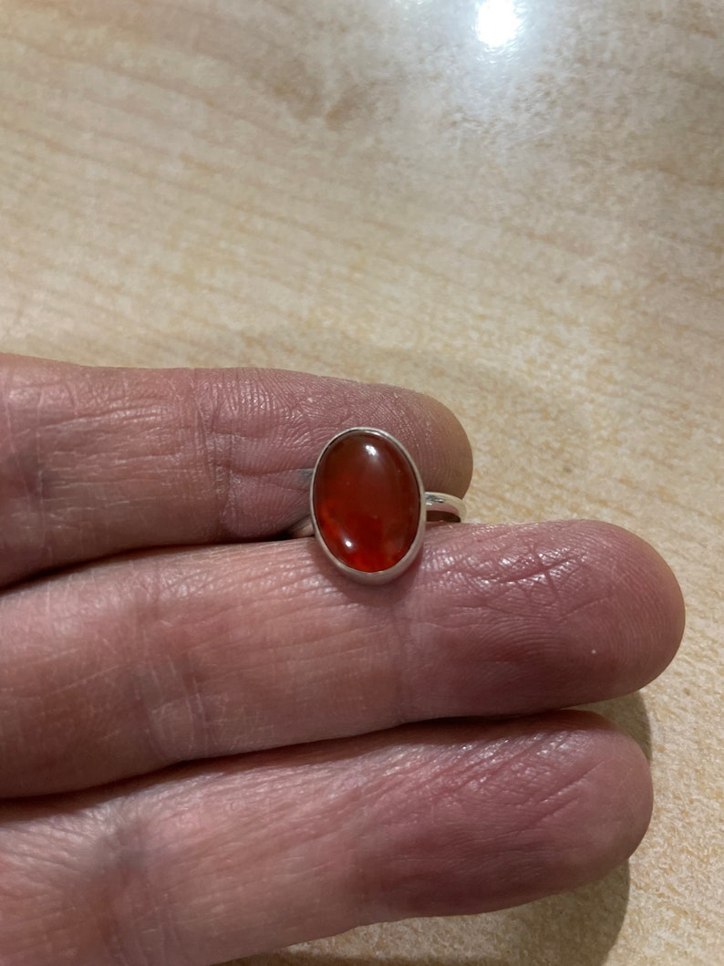 May include: A silver ring with an oval-shaped carnelian gemstone. The gemstone is a deep orange color.