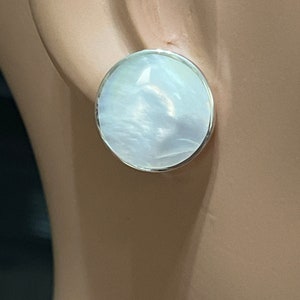 May include: A pair of white mother of pearl earrings with a silver setting. The earrings are round and have a smooth, polished finish.