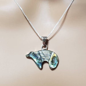 May include: A silver chain necklace with a bear pendant made of abalone shell. The bear is a stylized design with a green, blue, and gold iridescent finish.