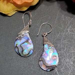 May include: A pair of silver earrings with iridescent abalone shell teardrop-shaped pendants. The earrings have a delicate silver wire design at the top.