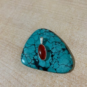 May include: A silver pendant with a red carnelian stone set in an oval shape.