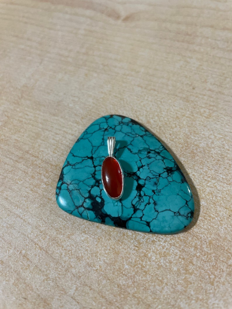 May include: A silver pendant with a red carnelian stone set in an oval shape.