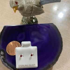 May include: A pair of sterling silver earrings with small red gemstones. The earrings are on a white card with the words "Sterling Silver" printed on it.