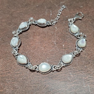 May include: A silver bracelet featuring pear-shaped, iridescent, white gemstones. The bracelet has a delicate chain design with a lobster clasp closure. The gemstones are set in ornate, silver bezels.