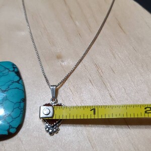 May include: A silver chain necklace with a heart-shaped pendant featuring a red gemstone. The pendant is approximately 1 inch in length.