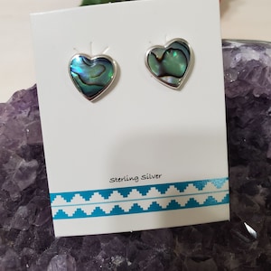 May include: A pair of sterling silver heart-shaped earrings with abalone shell inlays. The earrings are displayed on a white card with the text "Sterling Silver".