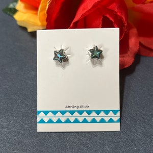 May include: A pair of sterling silver star-shaped earrings with a blue iridescent stone in the center. The earrings are displayed on a white card with a turquoise and white patterned border. The card also says "Sterling Silver".