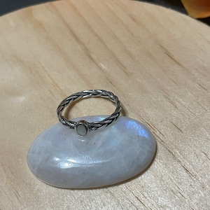 Peut inclure: Une bague en argent avec une bande tressée et une pierre ovale blanche.