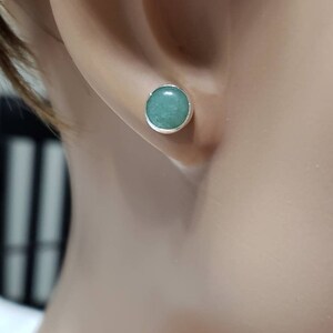 May include: A pair of silver stud earrings with a round, light green gemstone.