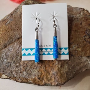 May include: A pair of sterling silver earrings with blue opal stones. The earrings are long and dangle. The stones are a light blue color with a shimmery finish.