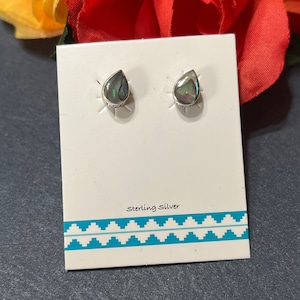 May include: A pair of sterling silver earrings with abalone shell teardrop-shaped stones. The earrings are displayed on a white card with a turquoise and white patterned border. The card also reads "Sterling Silver".