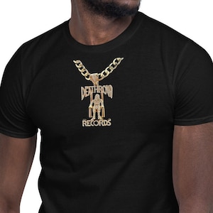 May include: A black t-shirt with a gold chain necklace featuring a pendant with the words "Death Row Records" in a stylized font.