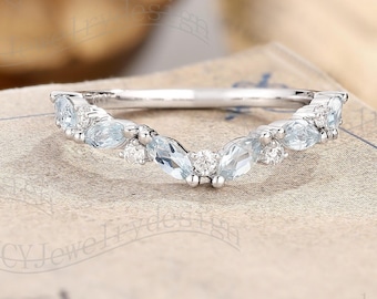 May include: A delicate silver band with a curved design featuring a row of marquise-shaped aquamarine gemstones and smaller round diamonds.