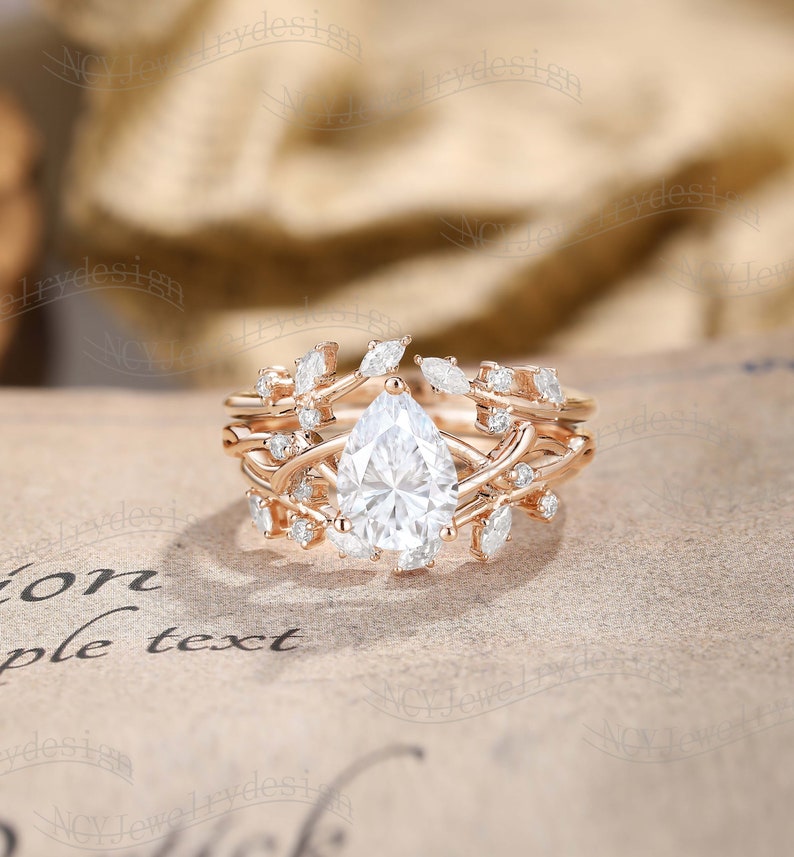 May include: A pear-shaped diamond engagement ring set in rose gold with a delicate floral design. The ring features a pear-shaped center stone surrounded by smaller diamonds and intricate floral details.