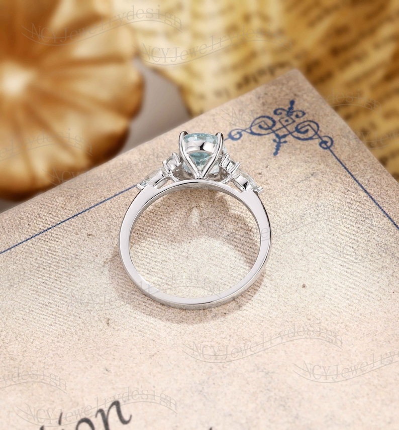 May include: A silver engagement ring with a light blue gemstone in the center and smaller gemstones on the band.